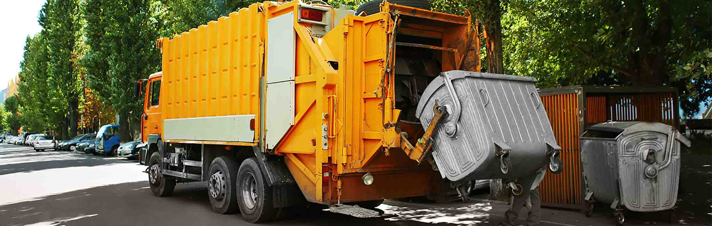 An orange garbage truck picking up a bin