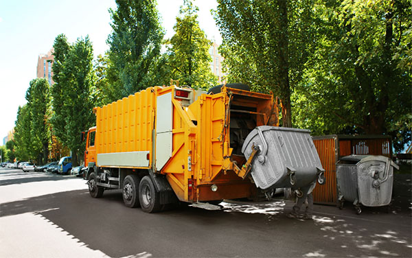 An orange garbage truck picking up a bin